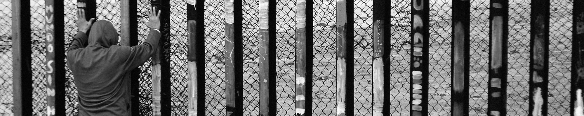 man with facing border fence with hands on it